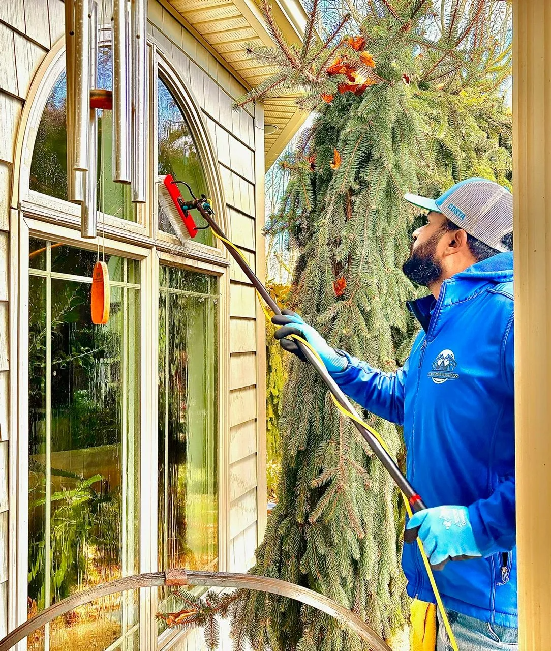 A professional technician using a water-fed extension pole and brush to clean residential window panes.
