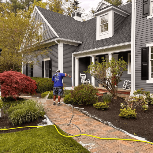 A professional technician soft washing the dark gray vertical siding and front porch entryway of a residential home.