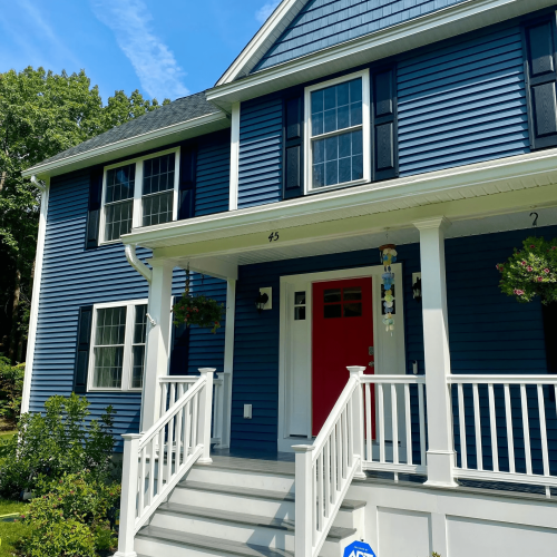 A gorgeous two-story residential home with clean blue horizontal siding, a red front door, and white porch trim.