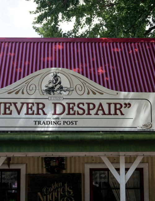 Front exterior of a commercial trading post building featuring a red metal roof and rustic wood signage.